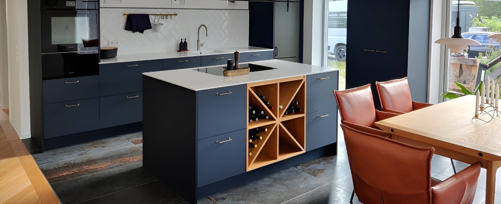 Eine moderne Küche mit marineblauen Schränken, einer weißen Arbeitsplatte, einem Weinkühlschrank und stilvollen Lederstühlen um einen Esstisch aus Holz.